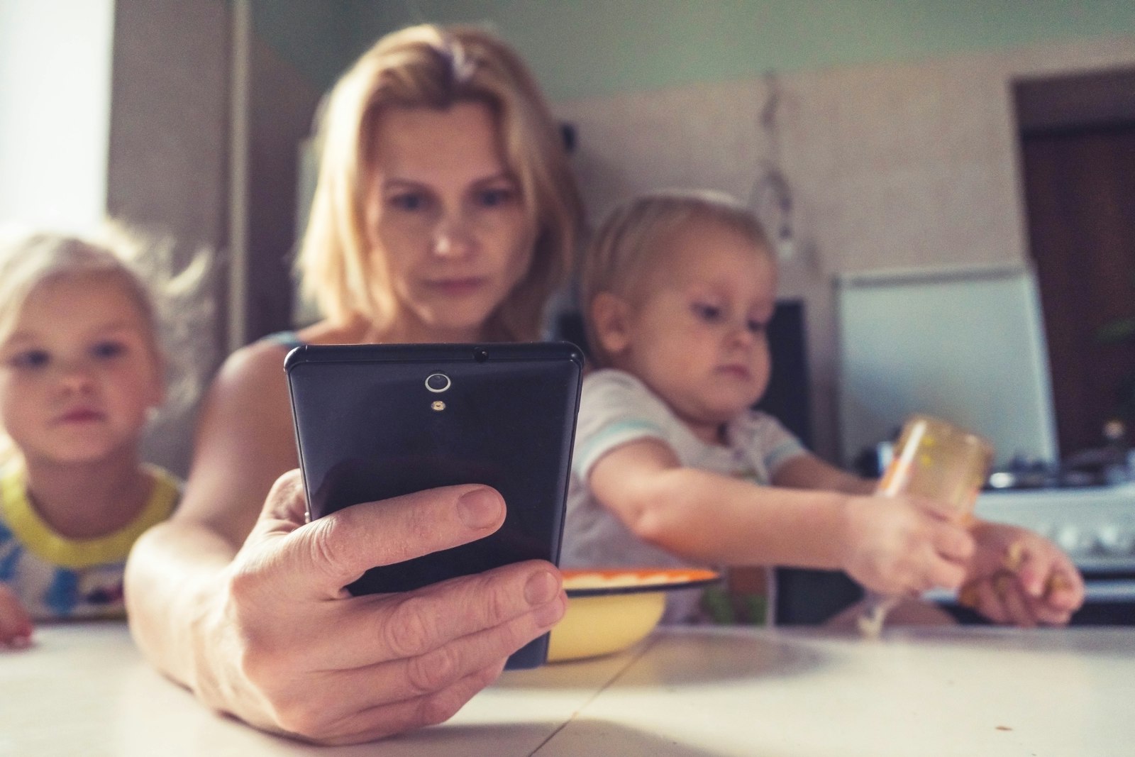 Мама працює зі смартфоном, сидячи поруч з дітьми